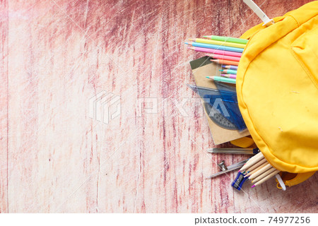 Top view of yellow backpack with different colorful stationery on table. Top view of yellow backpack with different colorful stationery on table. 74977256