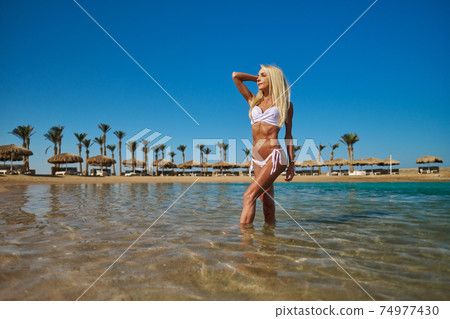 Young fashion woman standing in water on the beach Young fashion woman standing in water on the beach 74977430