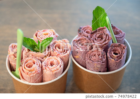 Duet of rolled ice creams decorated with fresh mint leaf in paper cups 74978422