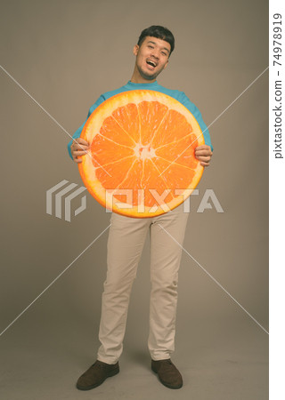 Portrait of young Asian man against gray background 74978919