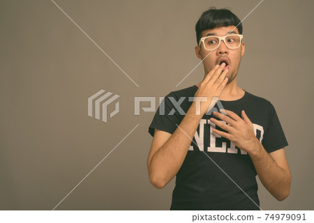 Young Asian nerd man wearing eyeglasses against gray background 74979091