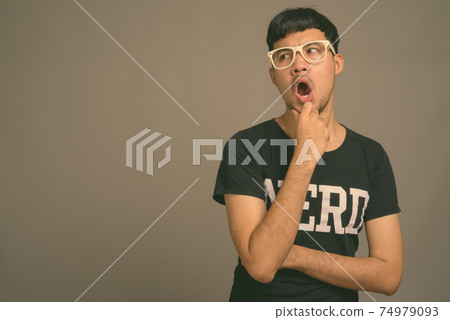 Young Asian nerd man wearing eyeglasses against gray background 74979093