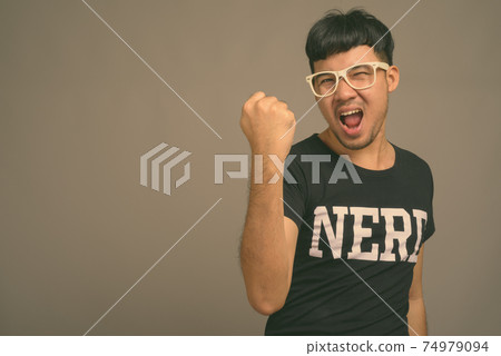Young Asian nerd man wearing eyeglasses against gray background 74979094