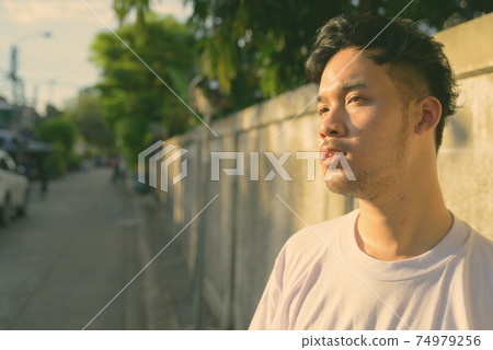 Young Asian man relaxing in the streets outdoors Young Asian man relaxing in the streets outdoors 74979256
