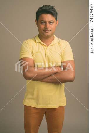 Portrait of young handsome Indian man against plain studio background Portrait of young handsome Indian man against plain studio background 74979450