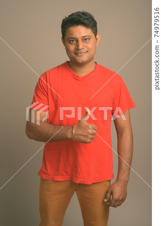 Portrait of young handsome Indian man against plain studio background 74979516