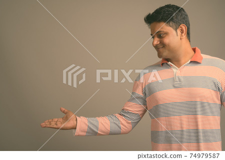 Portrait of young handsome Indian man against plain studio background 74979587