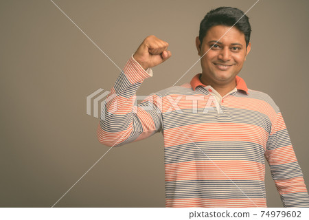 Portrait of young handsome Indian man against plain studio background 74979602