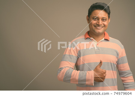 Portrait of young handsome Indian man against plain studio background 74979604