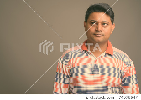 Portrait of young handsome Indian man against plain studio background Portrait of young handsome Indian man against plain studio background 74979647