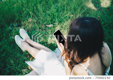 Beautiful women sitting on green grass use smartphone Beautiful women sitting on green grass use smartphone 74980140