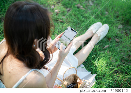 Beautiful women sitting on green grass use smartphone Beautiful women sitting on green grass use smartphone 74980143