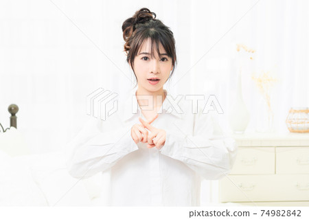 一件白襯衫，在房間裡做NG手勢的年輕女子 74982842