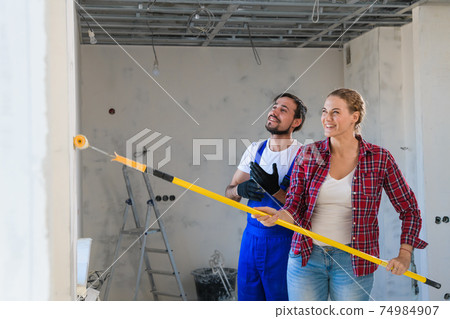 Woman helps repairer paint walls with paint roller 74984907