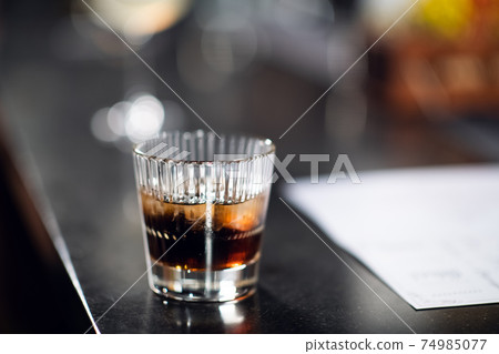 a glass of whiskey with ice on the bar close up 74985077