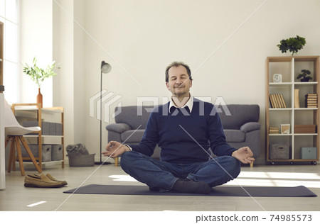 Man sitting on floor, meditating and enjoying moment of peace during busy work day Man sitting on floor, meditating and enjoying moment of peace during busy work day 74985573