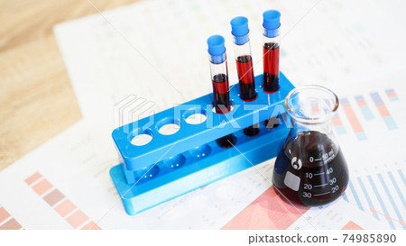 Test tubes on a stand and a flask with red blood on medical documents Test tubes on a stand and a flask with red blood on medical documents 74985890