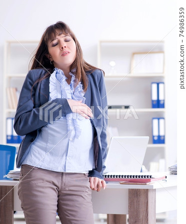Pregnant woman struggling to do work in office Pregnant woman struggling to do work in office 74986359