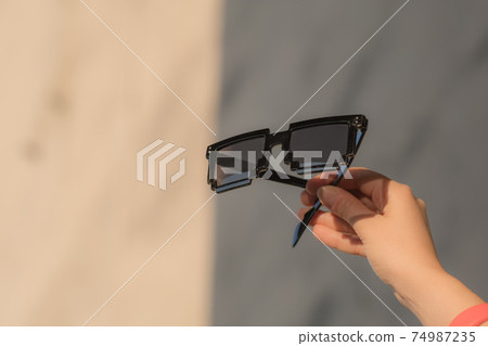 Black pixel sunglasses with black lenses hold by hand closeup in a sunny day. Selective focus Black pixel sunglasses with black lenses hold by hand closeup in a sunny day. Selective focus 74987235