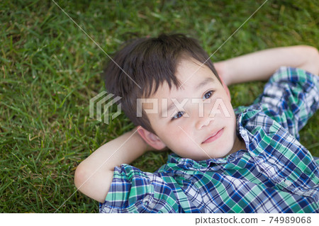 Thoughtful Mixed Race Chinese and Caucasian Young Boy Relaxing On His Back Outside On The Grass Thoughtful Mixed Race Chinese and Caucasian Young Boy Relaxing On His Back Outside On The Grass 74989068