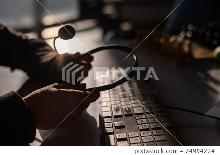 A woman is holding a headset with a microphone over a computer keyboard. Call center operator's workplace 74994224