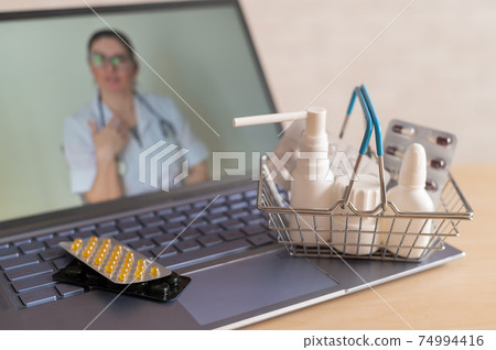 Video conference with a doctor on a laptop and tablet in a small shopping basket. Online pharmacy. Pharmacist on a computer screen. 74994416