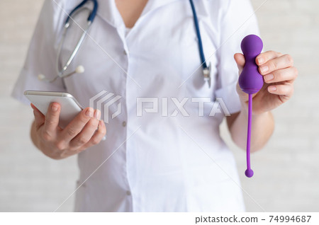 Unrecognized gynecologist recommends a kegel simulator to maintain women's health. The doctor synchronizes the vibrator with the smartphone. Device for the muscles of the pelvic floor. Unrecognized gynecologist recommends a kegel simulator to maintain women's health. The doctor synchronizes the vibrator with the smartphone. Device for the muscles of the pelvic floor. 74994687