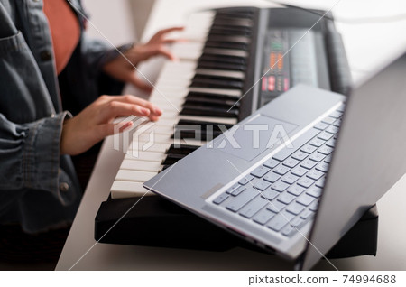 Close-up of female hands on the electric piano. A woman is learning to play the synthesizer on a laptop Close-up of female hands on the electric piano. A woman is learning to play the synthesizer on a laptop 74994688