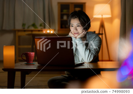 Young woman looking at a computer in the living room at night 74998093