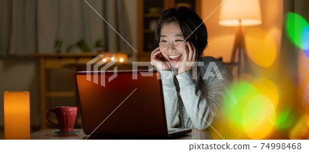 A smiling young woman looking at a computer in the living room at night Banner size 74998468