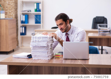 Young male employee unhappy with excessive work in the office Young male employee unhappy with excessive work in the office 75001759