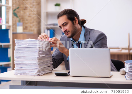 Young male employee unhappy with excessive work in the office Young male employee unhappy with excessive work in the office 75001933