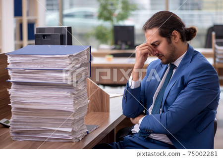 Young male employee unhappy with excessive work in the office Young male employee unhappy with excessive work in the office 75002281