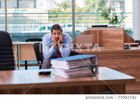 Young male employee unhappy with excessive work in the office Young male employee unhappy with excessive work in the office 75002592