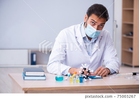 Young male chemist teacher sitting in the classroom Young male chemist teacher sitting in the classroom 75003267