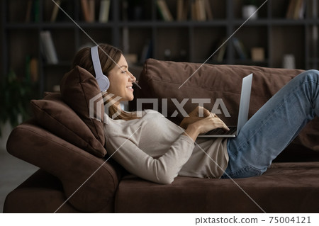 Smiling woman in headphones relax on sofa with laptop 75004121