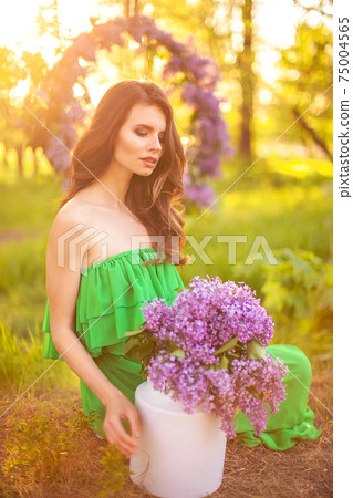 attractive woman in green dress posing near lilac flower 75004565