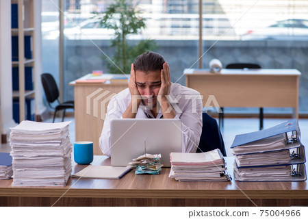 Young male employee unhappy with excessive work in the office Young male employee unhappy with excessive work in the office 75004966