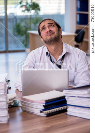 Young male employee unhappy with excessive work in the office 75005016