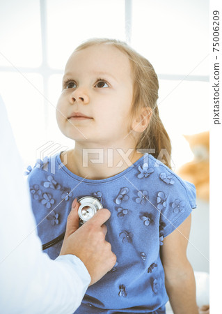 Doctor examining a little girl by stethoscope. Happy smiling child patient at usual medical inspection. Medicine and healthcare concepts Doctor examining a little girl by stethoscope. Happy smiling child patient at usual medical inspection. Medicine and healthcare concepts 75006209