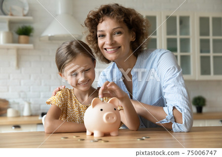 Happy smiling mom cuddling small girl putting coin to piggybank. Happy smiling mom cuddling small girl putting coin to piggybank. 75006747