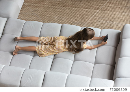 Top view of little girl lying on sofa using cell 75006809