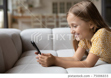 Smiling little child lying on couch look at phone screen Smiling little child lying on couch look at phone screen 75006833