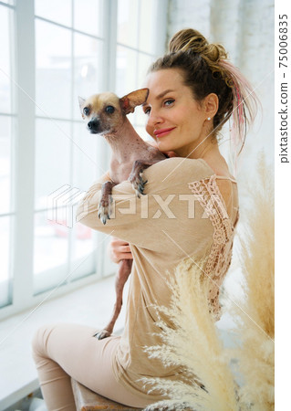 Happy adult woman hugging dog in room near big window 75006835