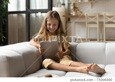 Smiling girl sit on sofa read book on tablet computer Smiling girl sit on sofa read book on tablet computer 75006980
