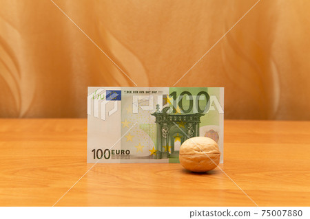 Walnut is in front of 100 euro. Curtains are golden. There is space around. The focus is on the money Walnut is in front of 100 euro. Curtains are golden. There is space around. The focus is on the money 75007880