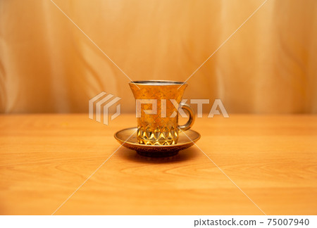 Golden cup for tea or coffee. On the golden background, orange table. Gold curtain. Cup in the center of the picture 75007940