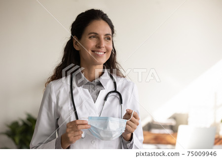 Head shot smiling female doctor holding medical face mask 75009946