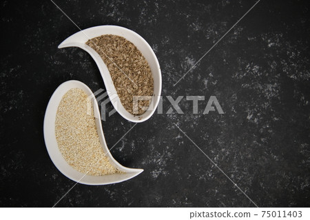 Dill and sesame seeds. Two plates in the form of a drop. Ying yan. On a gray background. Beat-up soft focus 75011403