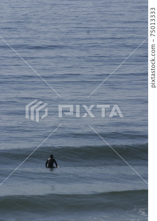 A surfer lying on his surfboard paddles over an approaching wave on a beach in Portugal on the Atlantic Ocean A surfer lying on his surfboard paddles over an approaching wave on a beach in Portugal on the Atlantic Ocean 75013333